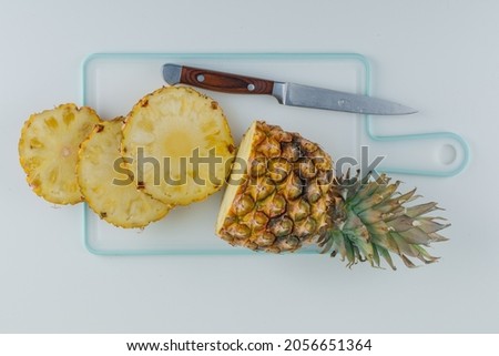 Sliced pineapple with knife flat lay on white and cutting board background 