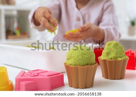 Little girl playing with bright kinetic sand at table indoors, focus on toys