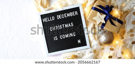 Christmas holiday framed border banner. On-trend stylish Christmas flat lay, cozy in bed or indoors with warm sweater, gifts and letter board spelling Hello December, Christmas is Coming.