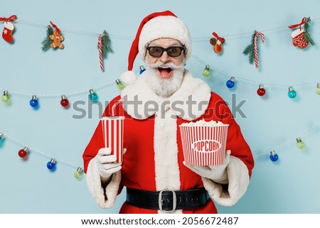 Young old man in 3d glasses Christmas hat red suit watch movie film hold bucket of popcorn cup of soda pop isolated on yellow background studio portrait. People emotions in cinema lifestyle concept