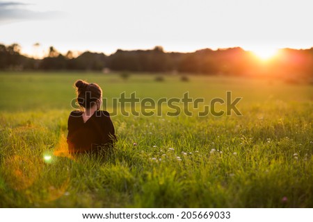 Portrait of a beautiful young woman or girl on very green meadow watching the sunset enjoying nature summer evening outdoors. Sunshine. Copy space. Royalty-Free Stock Photo #205669033