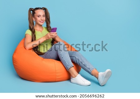 Full size photo of cute millennial lady sit on chair hold telephone wear jeans t-shirt footwear isolated on blue color background