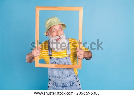 Photo of aged man happy positive smile curious interested look empty space wooden frame isolated over blue color background