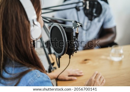 Multiracial hosts doing interview while streaming podcast together at record studio - Focus on microphone