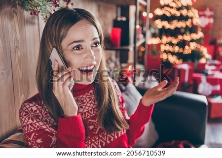 Photo of impressed shiny young woman dressed red sweater talking modern device new year greetings smiling indoors room home house