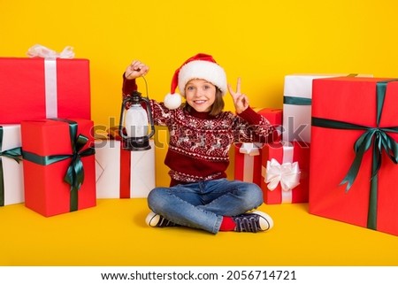 Full body photo of little small girl wear jeans hold lamp xmas v-sign good mood isolated on yellow color background