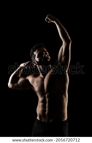 Side lit muscular Caucasian man silhouette. Athlete posing against black background. 