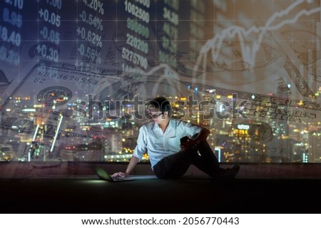 Asian businessman sitting and using the smart mobile phone showing the Stock market chart over Stack of coins and american dollars money over the LED display Stock market exchange data background