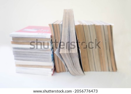A pile of  comic books, including a large collection of Japanese manga, is arranged neatly on a white background. The manga books feature intricate illustrations and captivating storylines