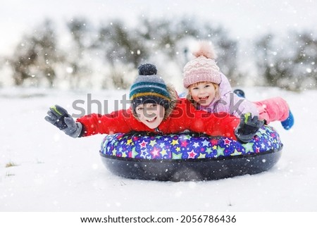 Active toddler girl and school boy sliding together down the hill on snow tube. Happy children, siblings having fun outdoors in winter on sledge. Brother and sister tubing snowy downhill, family time Royalty-Free Stock Photo #2056786436