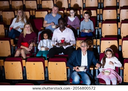 Interested adults with tween children absorbedly watching film in movie theater. Concept of joint leisure of parents and children