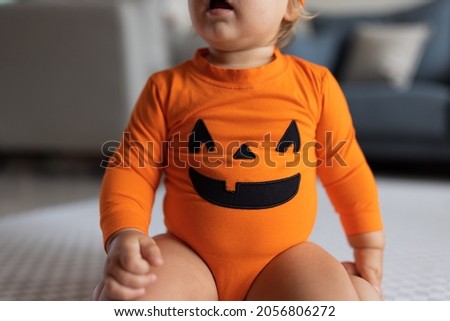 Cute caucasian infant baby Girl one year old in orange costume with pumpkin face at home. Happy Halloween concept