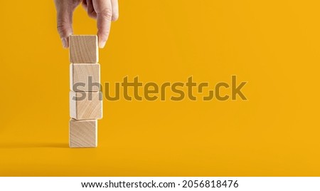 Square wooden blocks are stacked against each other on a yellow background, picking up the top wooden blocks to continue. Wooden block concept banner with copy space for text, poster, mockup template.