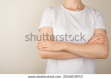 Cropped closeup photo of young woman in white t-shirt with crossed arms on isolated grey background with empty space