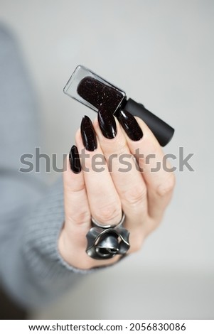 Woman's hands with long nails and black manicure with bottles of nail polish