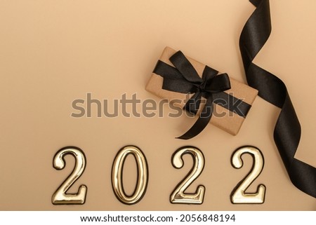 New Year 2022. Top view New Year mockup on beige background: black ribbon, gift box, golden numbers and multicolored sparkles. Layout of postcards, invitations.