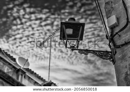 A black and white photo of a typical Spanish house facade in the old town of Felanitx on the Spanish island of Mallorca. An old lantern has a modern LED light. And antennas are in the picture.