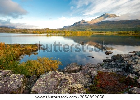 Mountain and sky reflecting in lake in early morning of autumn. Autumn colors in remote arctic landscape. Nieras mountain reflects in Lulealven dam in Stora Sjofallet national park, Sweden.