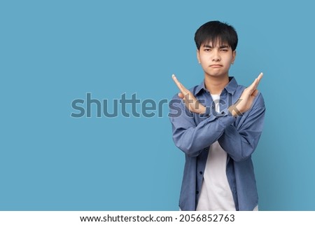 Portrait of young handsome Asian man showing STOP or Rejection expression crossing arms doing negative sign, angry face, isolated blue color background. Royalty-Free Stock Photo #2056852763