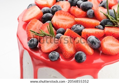 White cake covered with red icing, fresh strawberries and blueberries. Picture for a menu or a catalog of confectionery products. Macro photography.