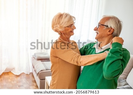 Carefree happy active old senior couple dancing jumping laughing in living room, cheerful retired elder husband holding hand of mature middle aged wife enjoy fun leisure retirement lifestyle at home