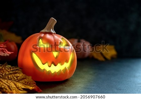 Halloween decorative pumpkin on dark background with autumn leaves