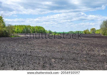 Plowed soil and green trees next to a field, agricultural landscape Royalty-Free Stock Photo #2056910597