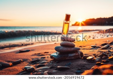 A transparent glass perfume bottle with a gold lid hovers over a pyramid of stones. Sandy beach and sunset in the background. Copy space. Perfume advertising concept. Royalty-Free Stock Photo #2056919672