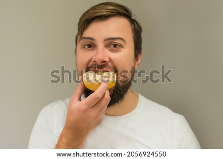 Young bearded handsome man in a white T-shirt holds homemade cakes donuts bites on a gray background. Concept: Celebrating Happy Birthday Donut Celebration 