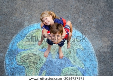 Little preschool girl and school kid boy with earth globe painting with colorful chalks on ground. Happy earth day concept. Creation of children for saving world, environment and ecology. Royalty-Free Stock Photo #2056927895