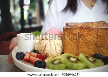 Woman served Chocolate chip ice cream with toasted bread, served with sliced kiwi and whipping cream. Dessert set on plate. Selective focus and free space for text. Toned image.