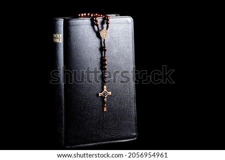 Bible with wooden rosary beads and crucifix isolated on a black background