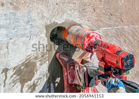 Worker is drilling to concrete wall with core drill machine. Core drills used in metal are called annular cutters. Core drills used for concrete and hard rock generally use industrial diamond grit. Royalty-Free Stock Photo #2056961153