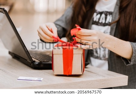 The woman opens the gift. There is a laptop and a credit card on the table. Online shopping and gift concept. Horizontal photo