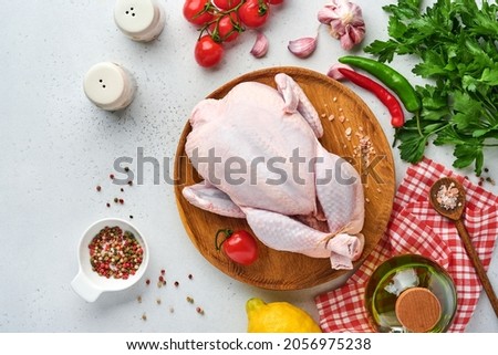 Whole raw chicken with ingredients for making rose pepper, lemon, thyme, garlic, cherry tomato, sorrel and salt in the kitchen on light grey slate stone or concrete background Top view with copy spac Royalty-Free Stock Photo #2056975238
