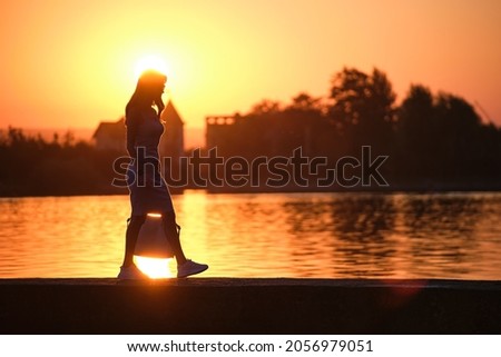 Young woman in casual outfit walking on lake side on warm evening. Summer vacations and travelling concept.
