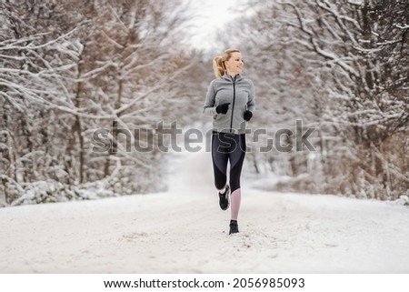 Full length of happy middle-aged sportswoman running in nature at snowy winter day. Outdoor fitness, cardio exercises, exercises in nature Royalty-Free Stock Photo #2056985093