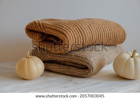Bunch of knitted warm pastel color sweaters with different knitting patterns folded in stack, visible texture. Stylish fall-winter season knitwear with pumpkin on top. Close up, copy space for text.