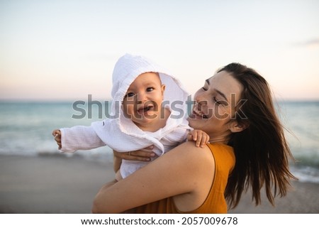 Mom holds her son in her arms. Mother and the child meets the sunset on the sea. pastime of mom and son. Happy motherhood. Mom and son relationship.