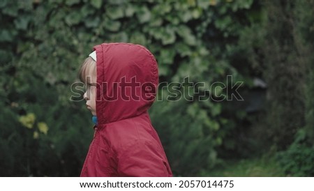 Sad girl in a hood on the background of green foliage