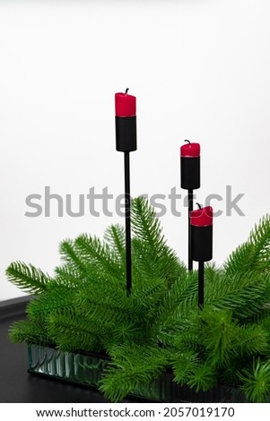 Red candles decorated with an artificial Christmas tree are on a white background . High quality photo