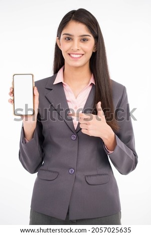 Woman Pointing Finger At Smartphone Blank Screen Standing On White Studio Background.