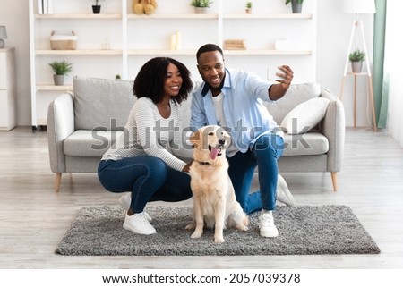 Smiling black woman and man taking selfie together with pet at home, looking at telephone camera, happy family having fun, laughing making photo posing for selfportrait picture sitting on floor carpet