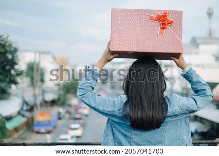Long hair girl hold gift box on her head turn back. On city sky view.