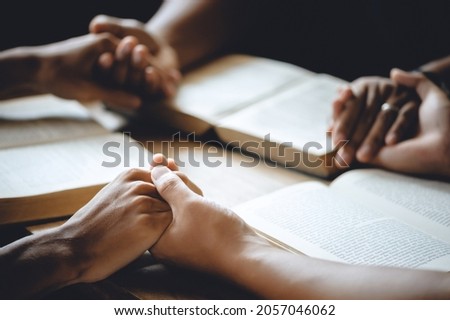 Christian group of people holding hands praying worship to believe and Bible on a wooden table for devotional or prayer meeting concept. Royalty-Free Stock Photo #2057046062
