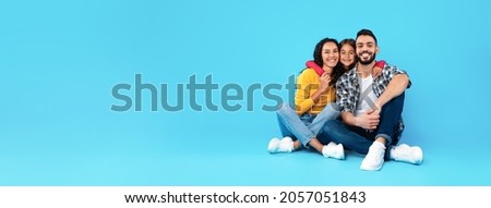 Middle-Eastern Parents and Daughter Embracing On Blue Background Posing Together In Studio, Sitting Near Empty Space For Text Advertisement. Great Family Offer Concept. Panorama
