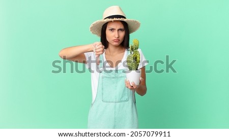 pretty farmer woman feeling cross,showing thumbs down and holding a cactus