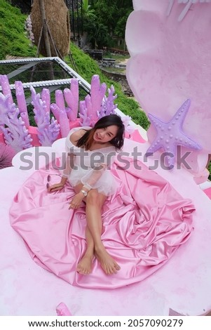A beautiful girl in a good mood sits on a pink seashell seat on a weekend's rest.