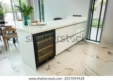 White kitchen island granite countertops and white drawer cabinet, Have modern black Built in wine refrigerator under countertop. Beautiful white marble floor tiles. Royalty-Free Stock Photo #2057094428