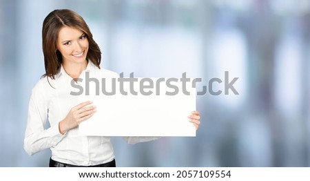 Happy smiling woman in white confident wear holding showing mock up empty signboard. Businesswoman in advertising studio ad concept. Copy space area. Blurred modern office background.	Female executive